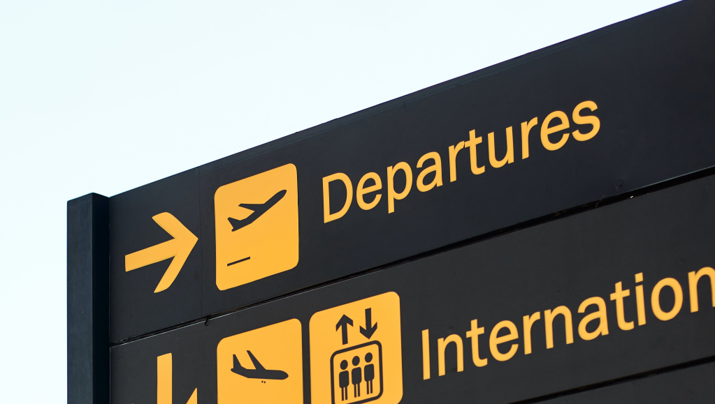 Un panneau d’indication d’aéroport indiquant la direction des départs (il y a écrit « departures » à côté d’un icône d’avion qui décolle)